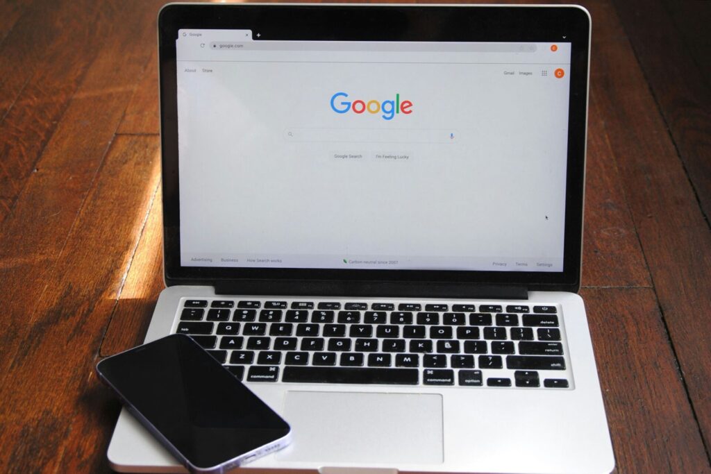 open laptop on wooden surface with cell phone resting on keyboard. Google search engine window pulled up on screen