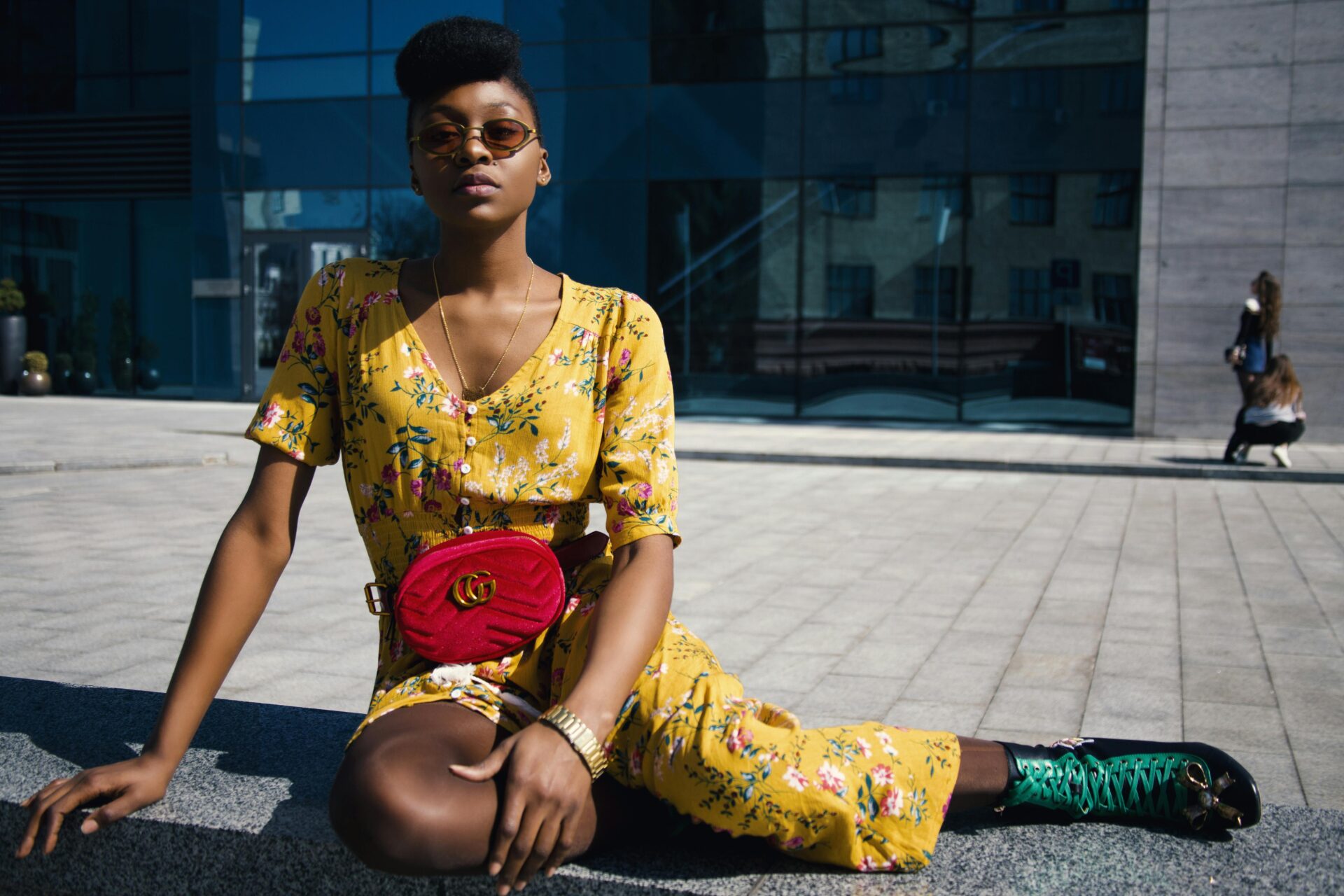 Girl wearing yellow dress and green boots with red Gucci bag, sitting on ground